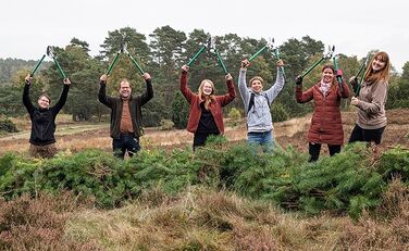 Lünestrom-Mitarbeiterinnen stehen mit einem VNP-Mitarbeiter in der Heide und recken Astscheren in die Höhe.